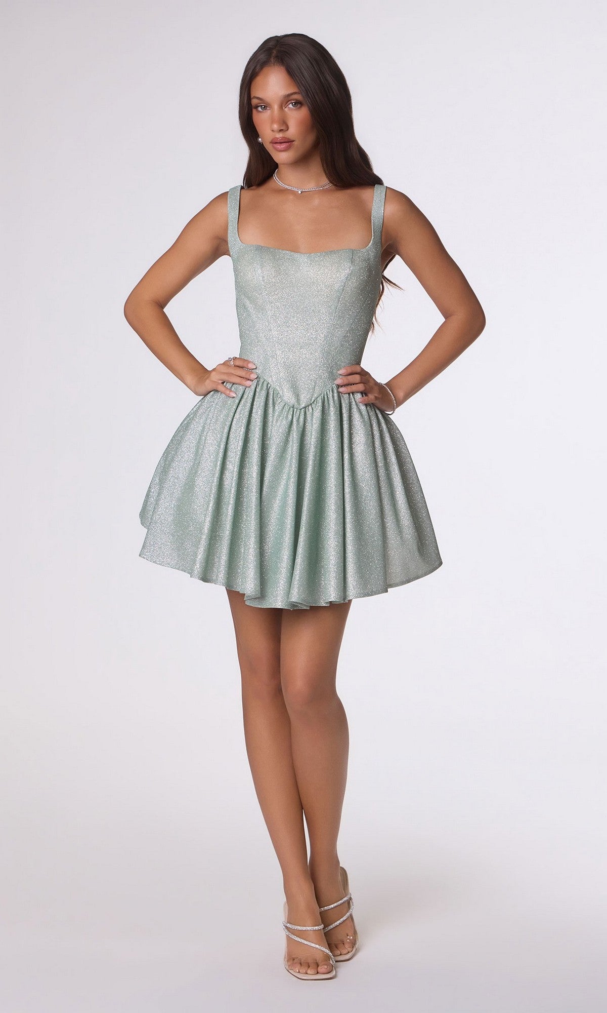 A woman models the Amoris T738 short homecoming dress, featuring a sleeveless fit-and-flare design in shimmering stretch fabric and light green color, set against a plain white background.